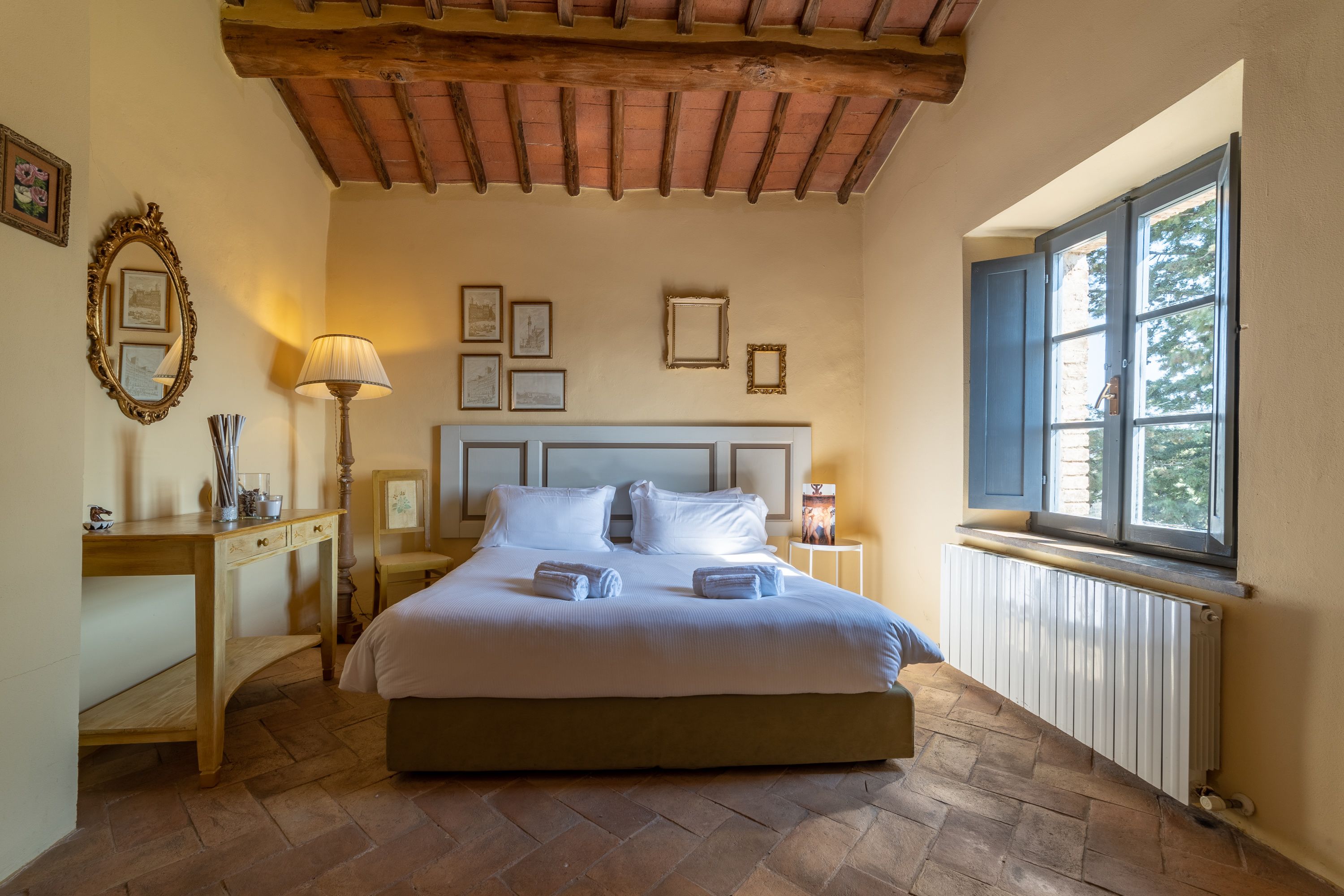 A bedroom with a wooden bed, a nightstand, a lamp, and a window with a view of trees.