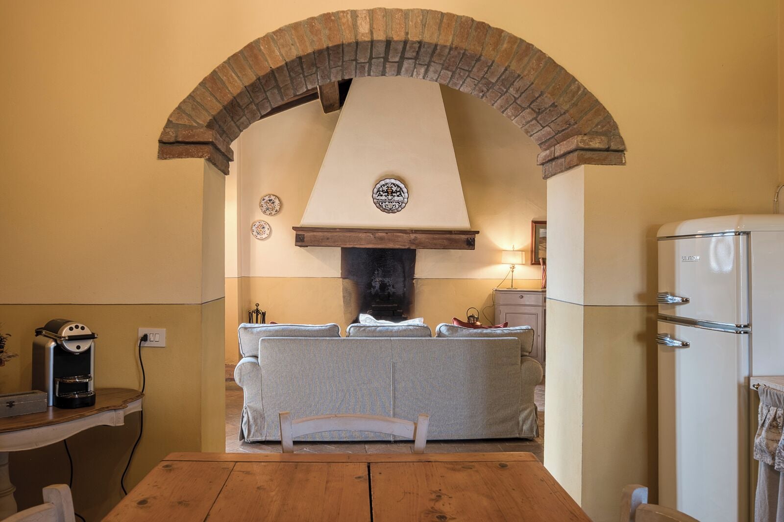 Une cuisine avec une arche en briques, un four encastré, un réfrigérateur et une table à manger.