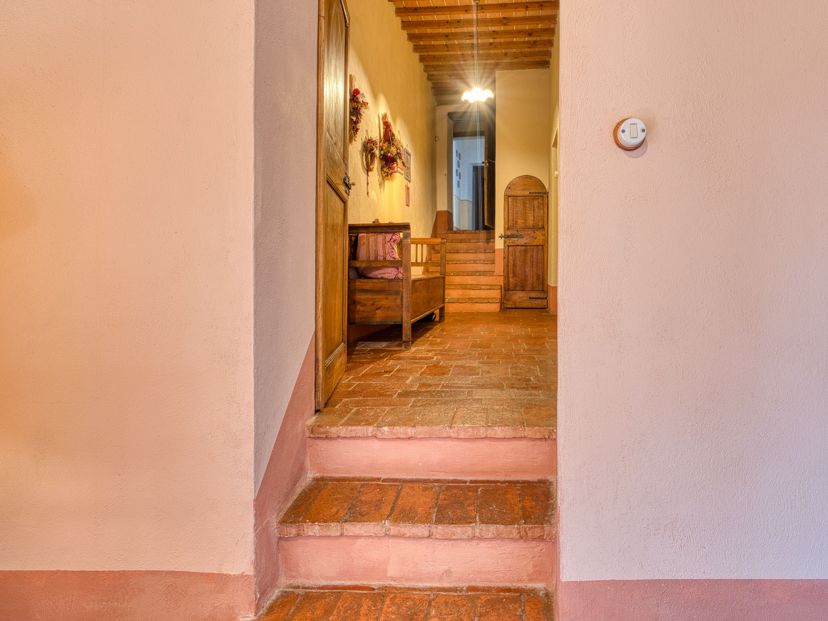 A narrow staircase leading to a room with a wooden door, a small bench, and a wall-mounted light fixture.