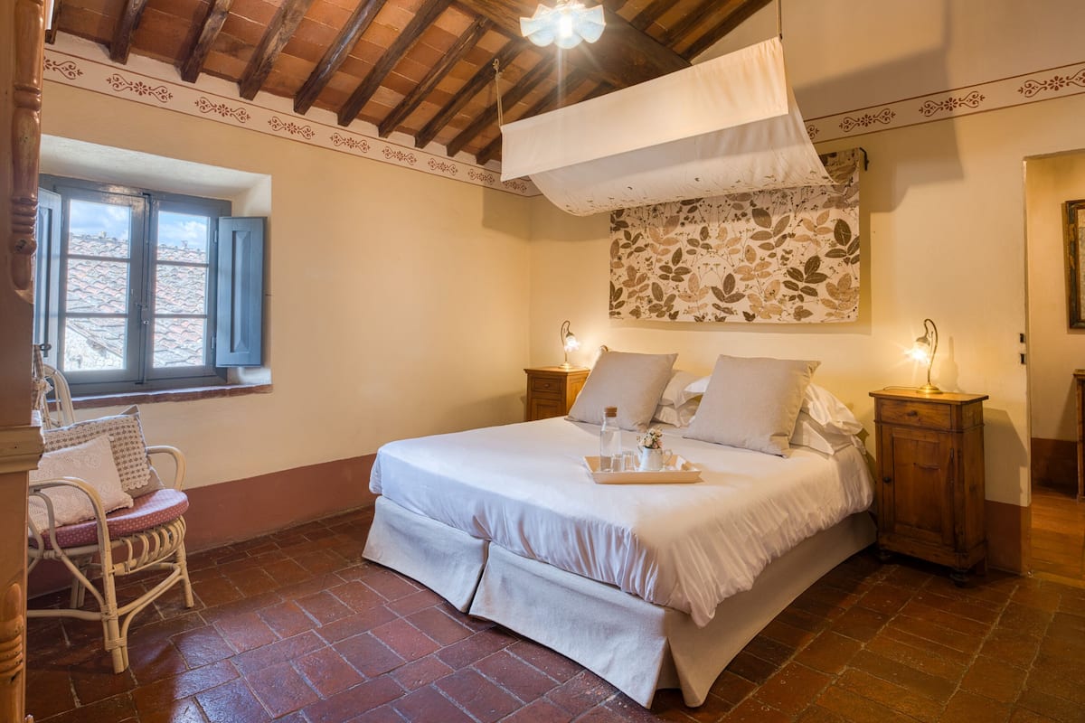 A bedroom with a bed, a nightstand, a chair, a window, and a decorative wall piece.