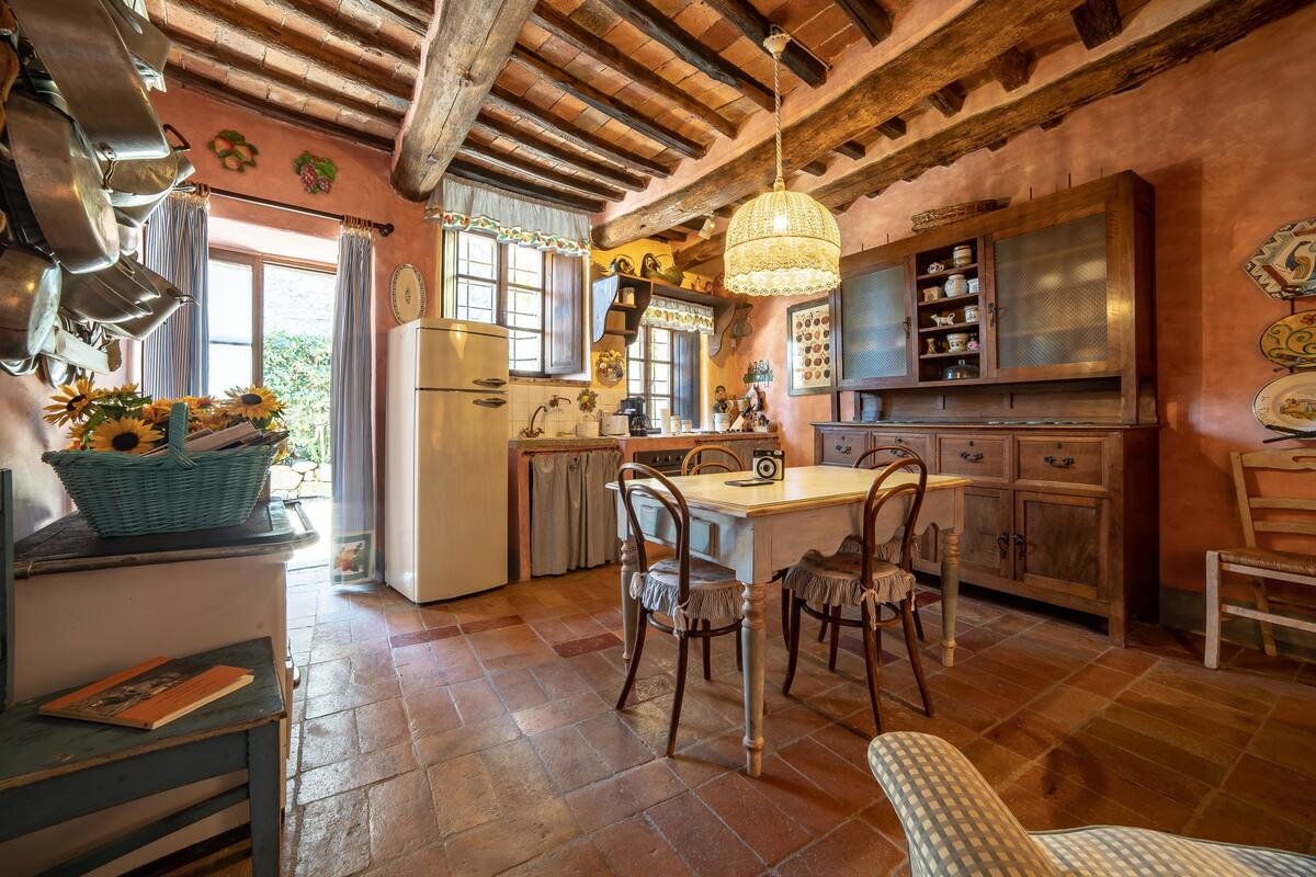 A rustic kitchen with exposed wooden beams, a large island with chairs, and a hanging light fixture.