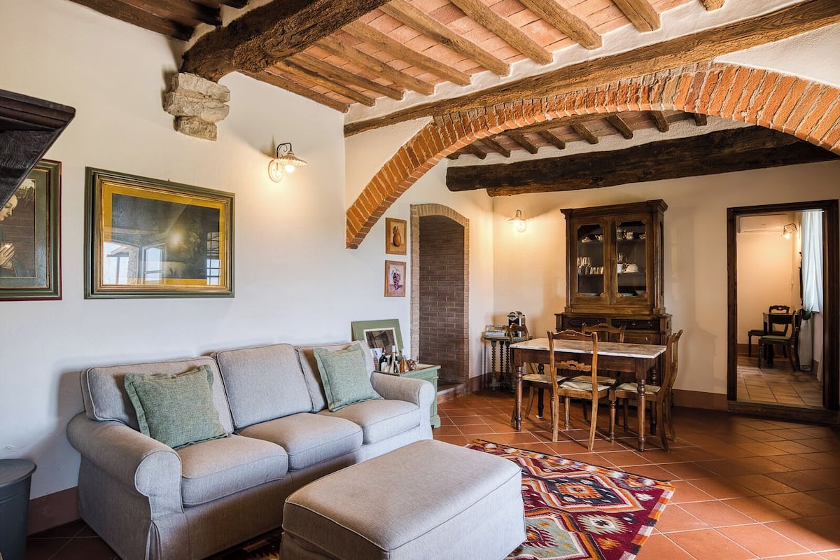 A cozy living room with a sofa, a patterned rug, and a dining area with a wooden table and chairs.