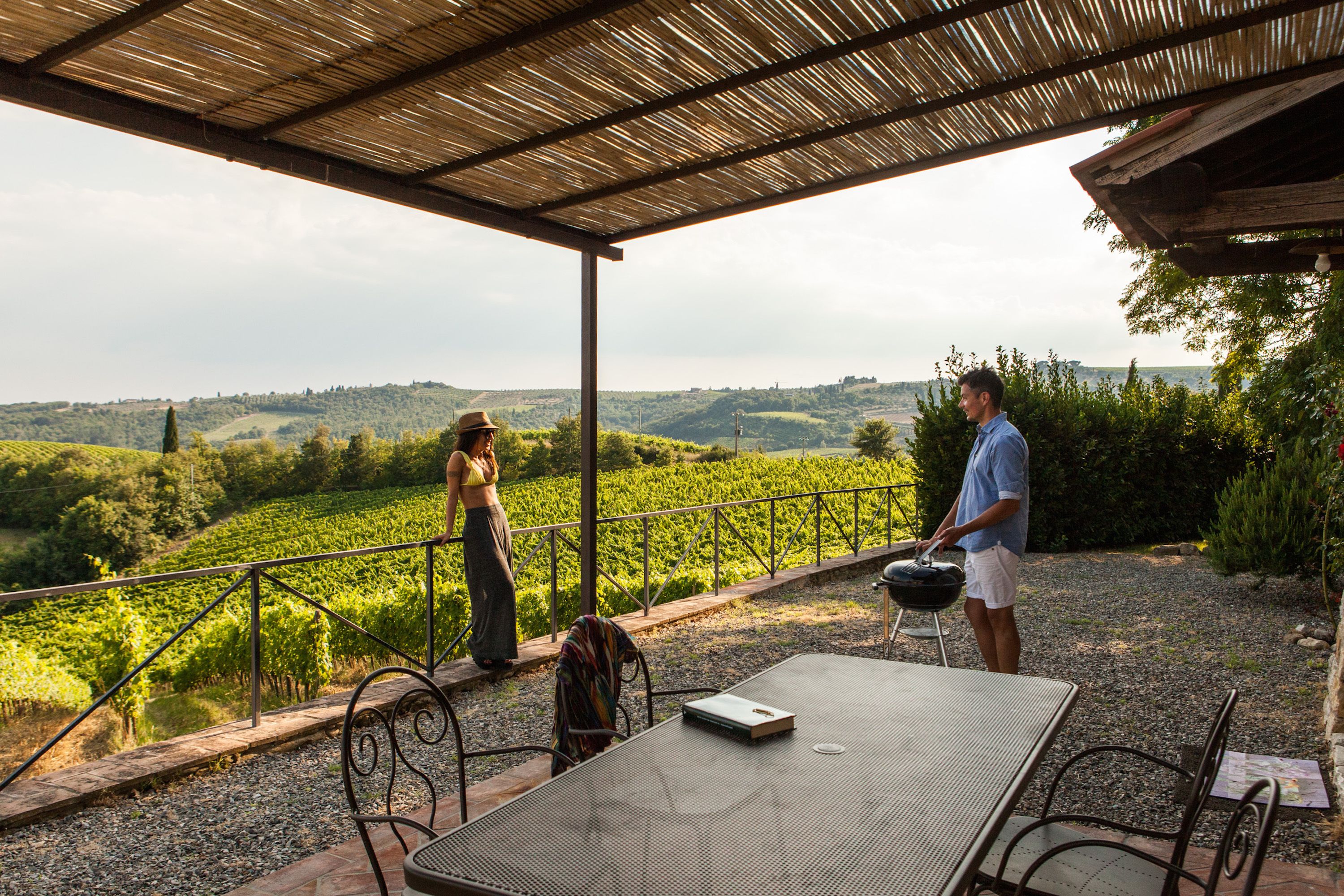 An outdoor patio with a table and chairs, a grill, and a view of a vineyard.