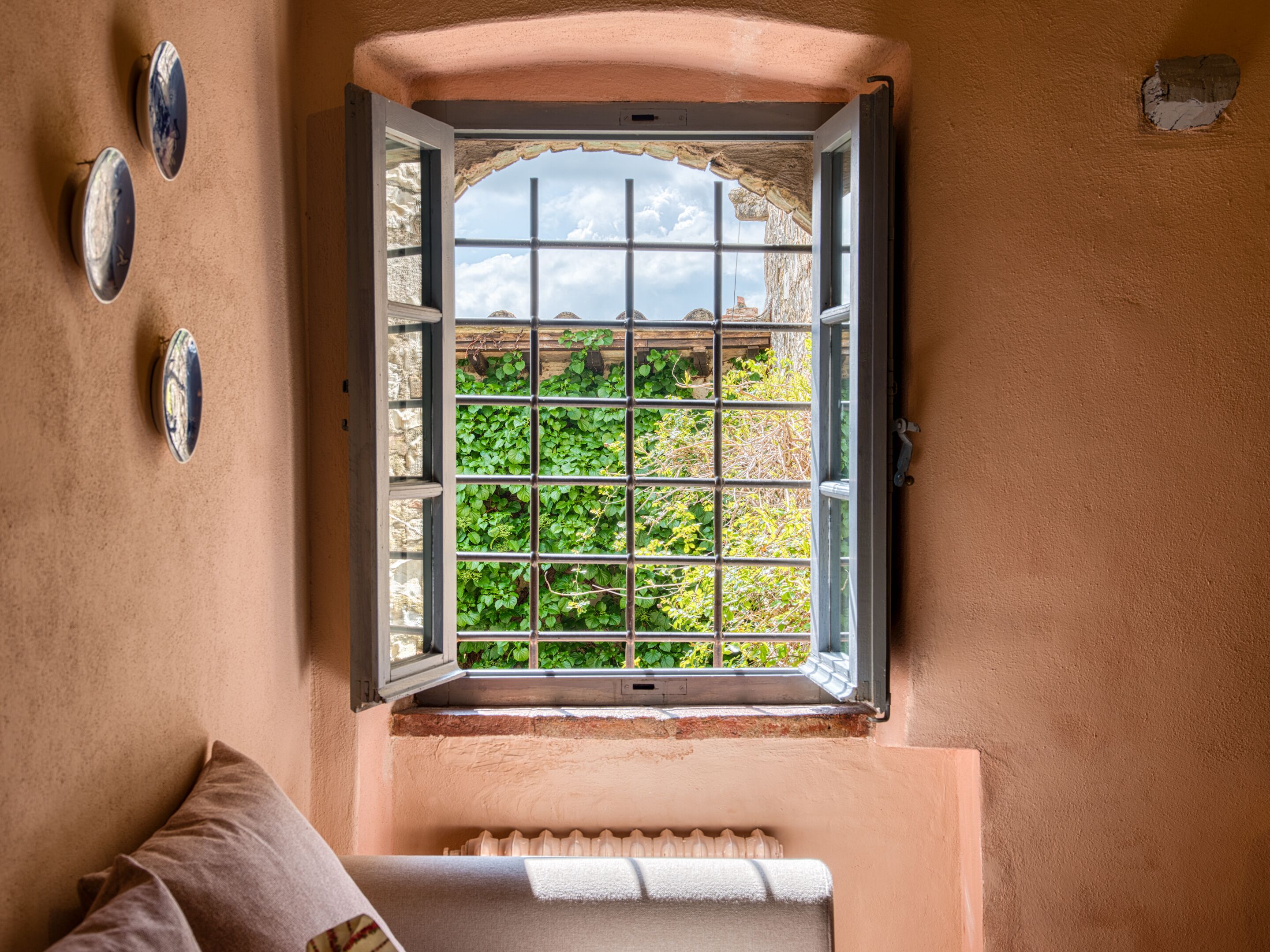 Una habitación con ventana que da a un jardín, un radiador debajo de la ventana y un espejo colgado en la pared.