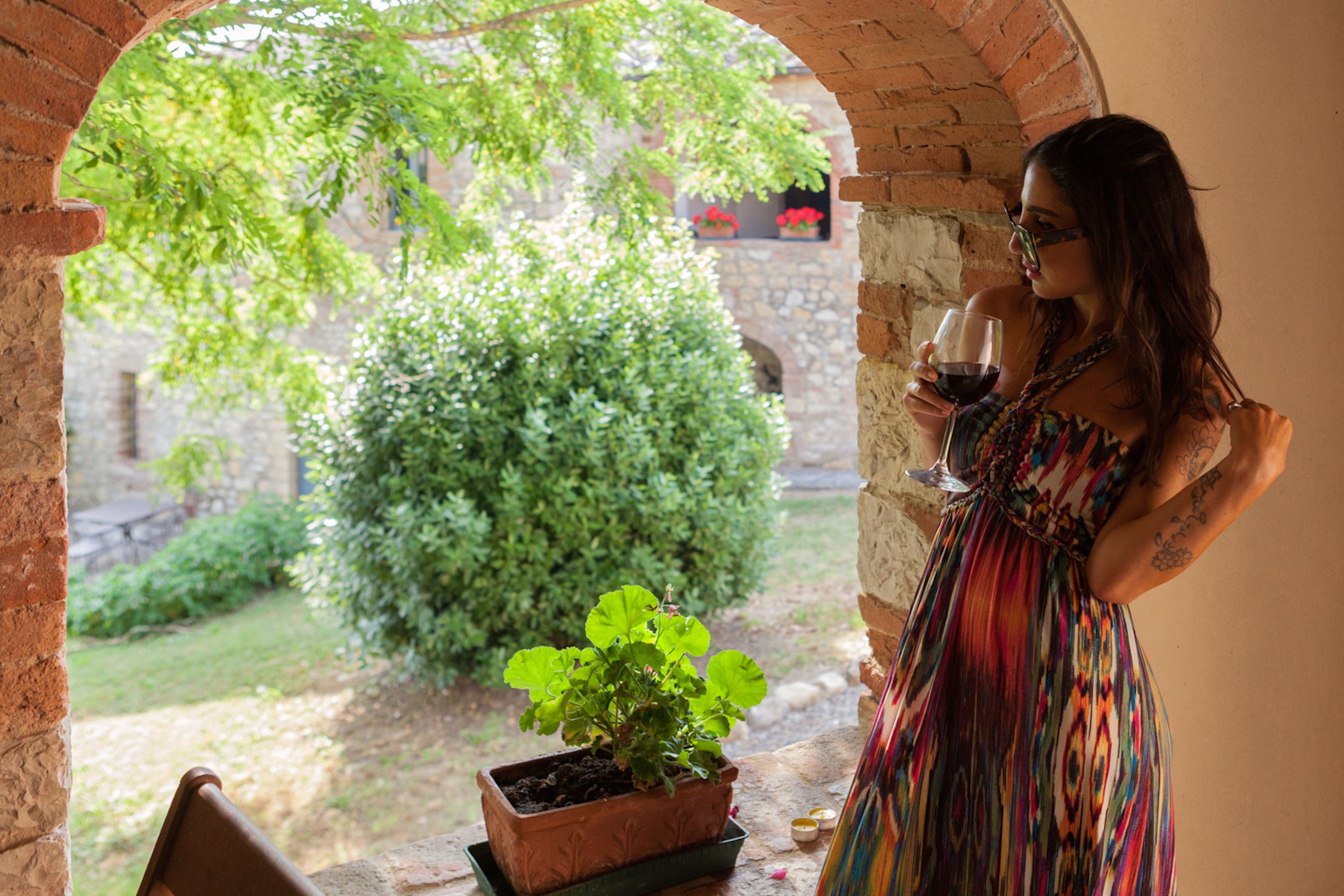 A woman standing in a courtyard with a potted plant and a wine glass.