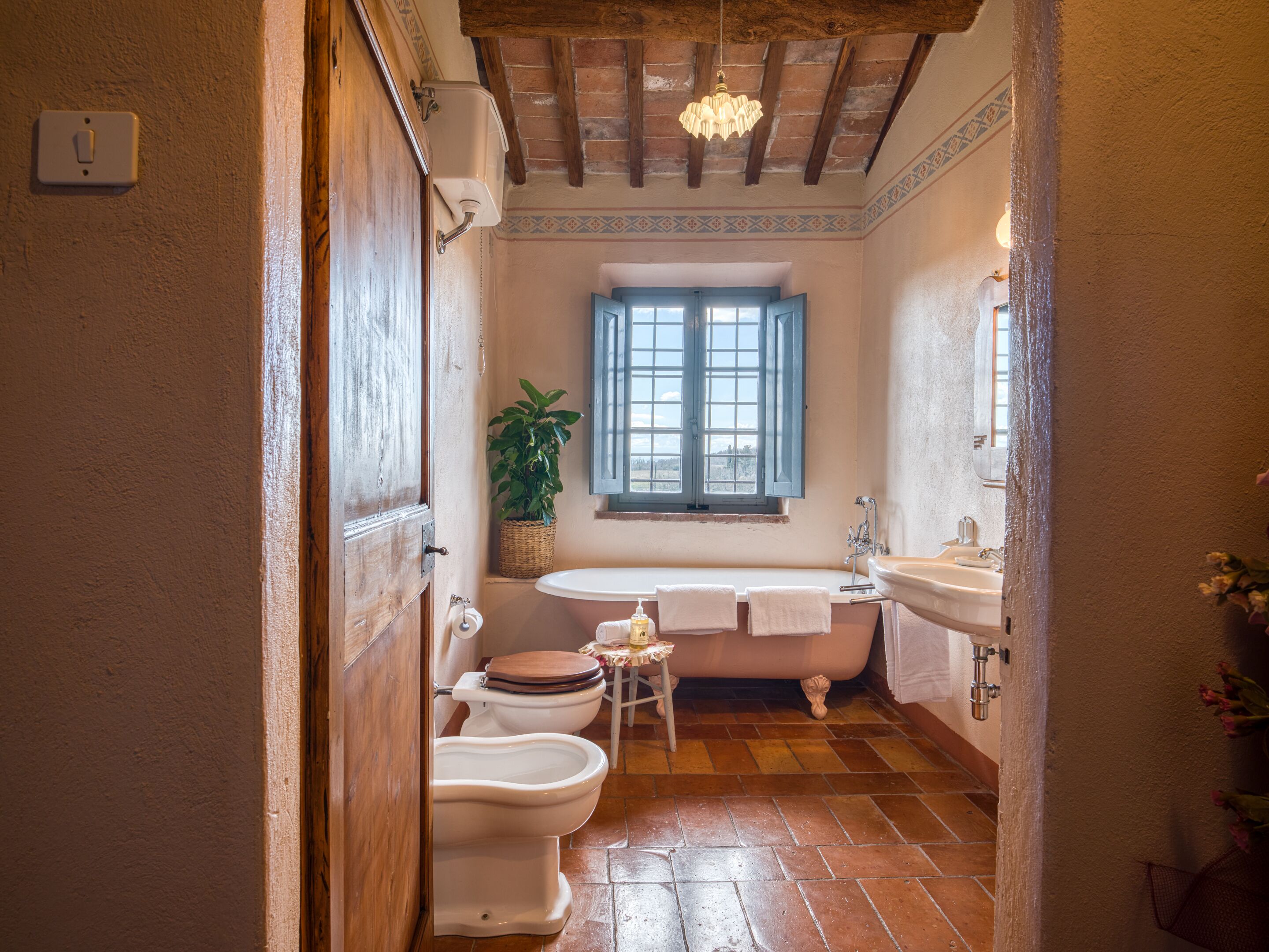 Une salle de bain avec un plancher en bois, une fenêtre, un lavabo et deux toilettes.