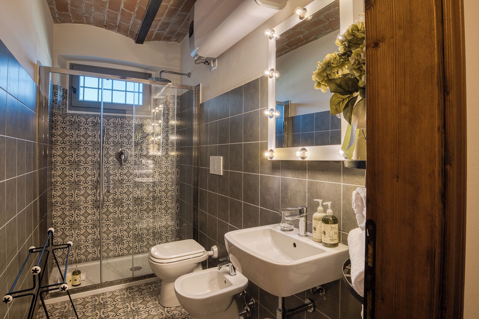 Ein Badezimmer mit Dusche, Toilette, Bidet, Waschtisch und einem beleuchteten Spiegel.