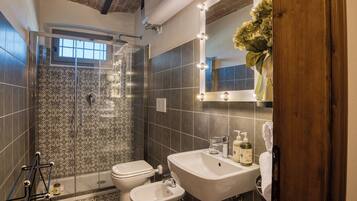 Ein Badezimmer mit Dusche, Toilette, Bidet, Waschtisch und einem beleuchteten Spiegel.