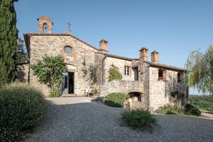 Un edificio de piedra con una torre de campanas, ventanas de arco y un camino de grava.