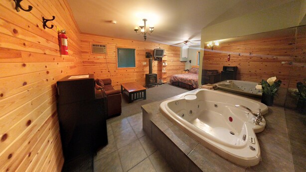 A log cabin interior with a large bathtub, a fireplace, and a television.
