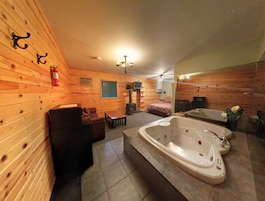 Interior de una cabaña de madera con una bañera grande, una chimenea y un televisor.