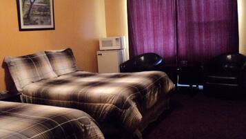 A hotel room with two beds, a desk, a chair, a microwave, and a painting on the wall.