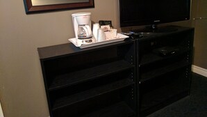 A hotel room with a flat-screen TV, a coffee maker, and a tray with cups and a bottle.