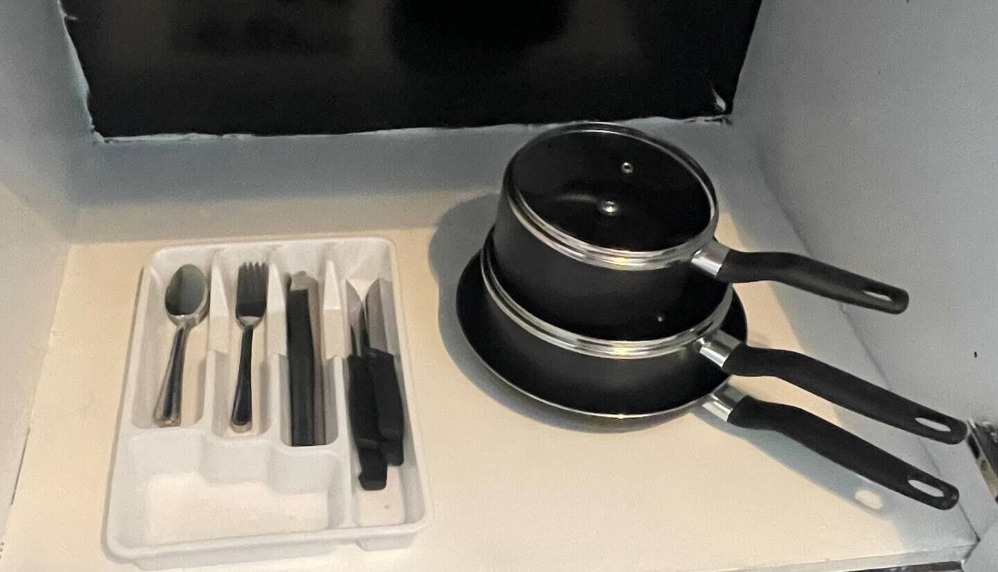 Un área de cocina con una olla negra sobre la estufa, un juego de utensilios en un recipiente blanco, y una caja negra al fondo.