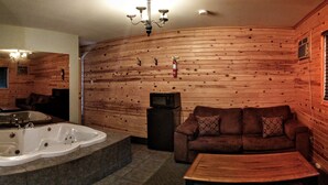 A wooden interior with a large bathtub, a sofa, and a television.