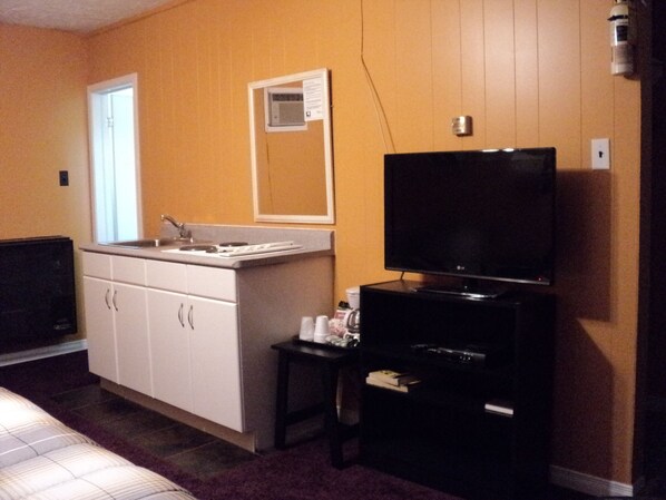 A hotel room with a bed, a TV, a small table with a remote control, a sink, and a mirror on the wall.