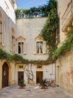 Pátio com bicicleta, plantas em vasos e um edifício com a placa 'Corte & Rimoniti'.