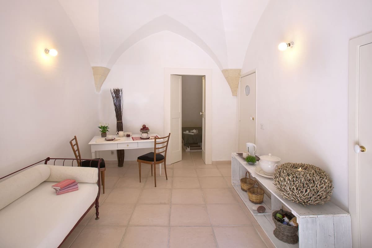 A cozy room with a white sofa, a dining table with chairs, a small kitchen area, and a door leading to another room.