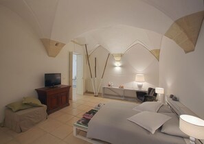 Un dormitorio con cama, mesita de noche, lámpara, escritorio, silla, televisor y ventana.