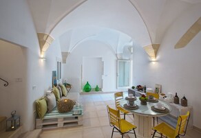 Uma sala de jantar espaçosa com mesa de vidro, cadeiras amarelas e teto branco com arcos.