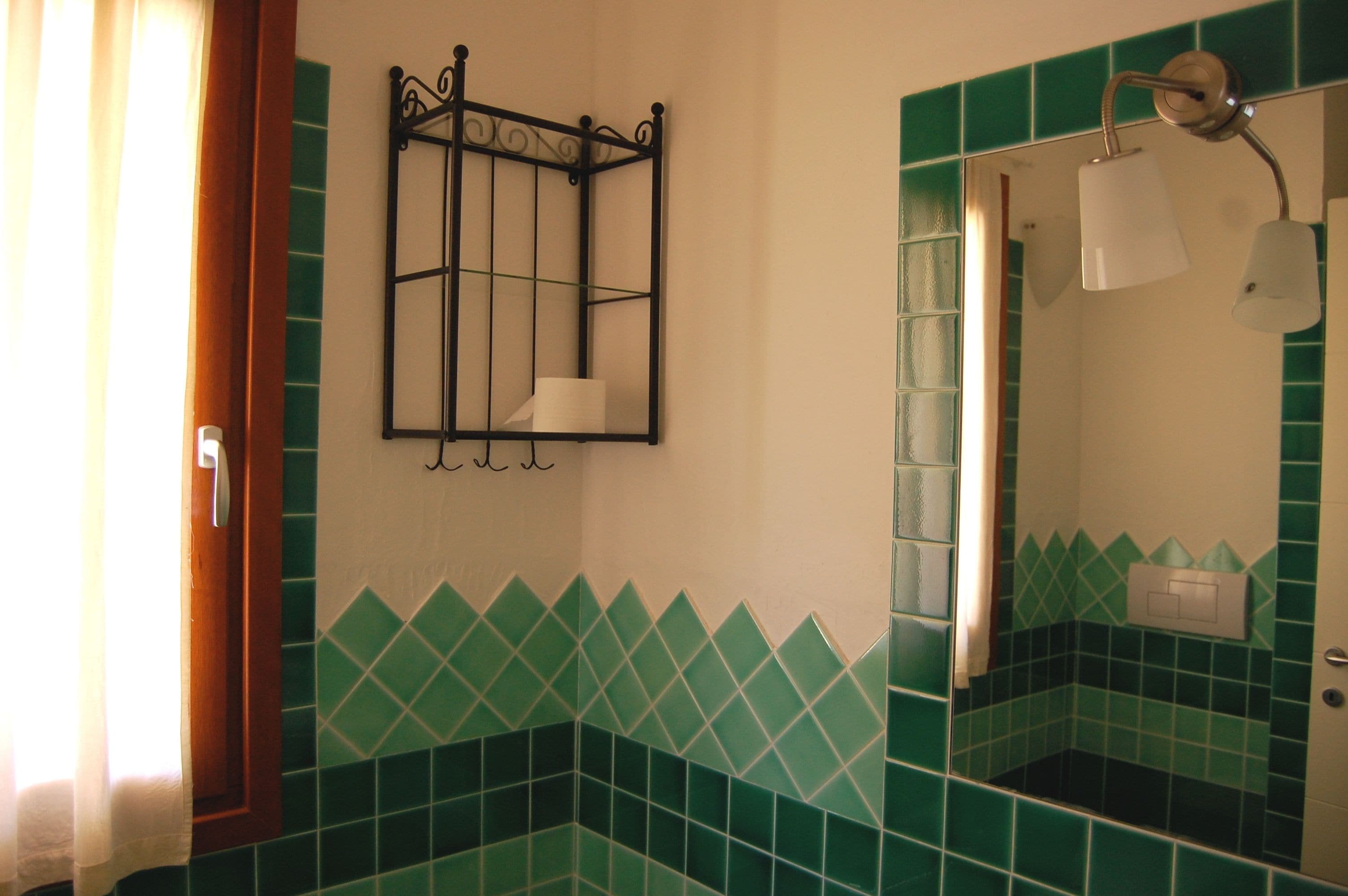 A bathroom with green-tiled walls, a mirror, a towel rack, and a shower with a light fixture.