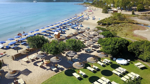 An aerial view of a beach with rows of umbrellas and sun loungers, a grassy area with tables, and a clear view of the sea. - Le Saline Palau (Palau)