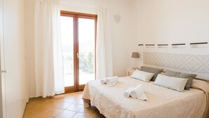 A bedroom with a bed, pillows, a nightstand, a lamp, and a view through a door. - Le Saline Palau (Palau)