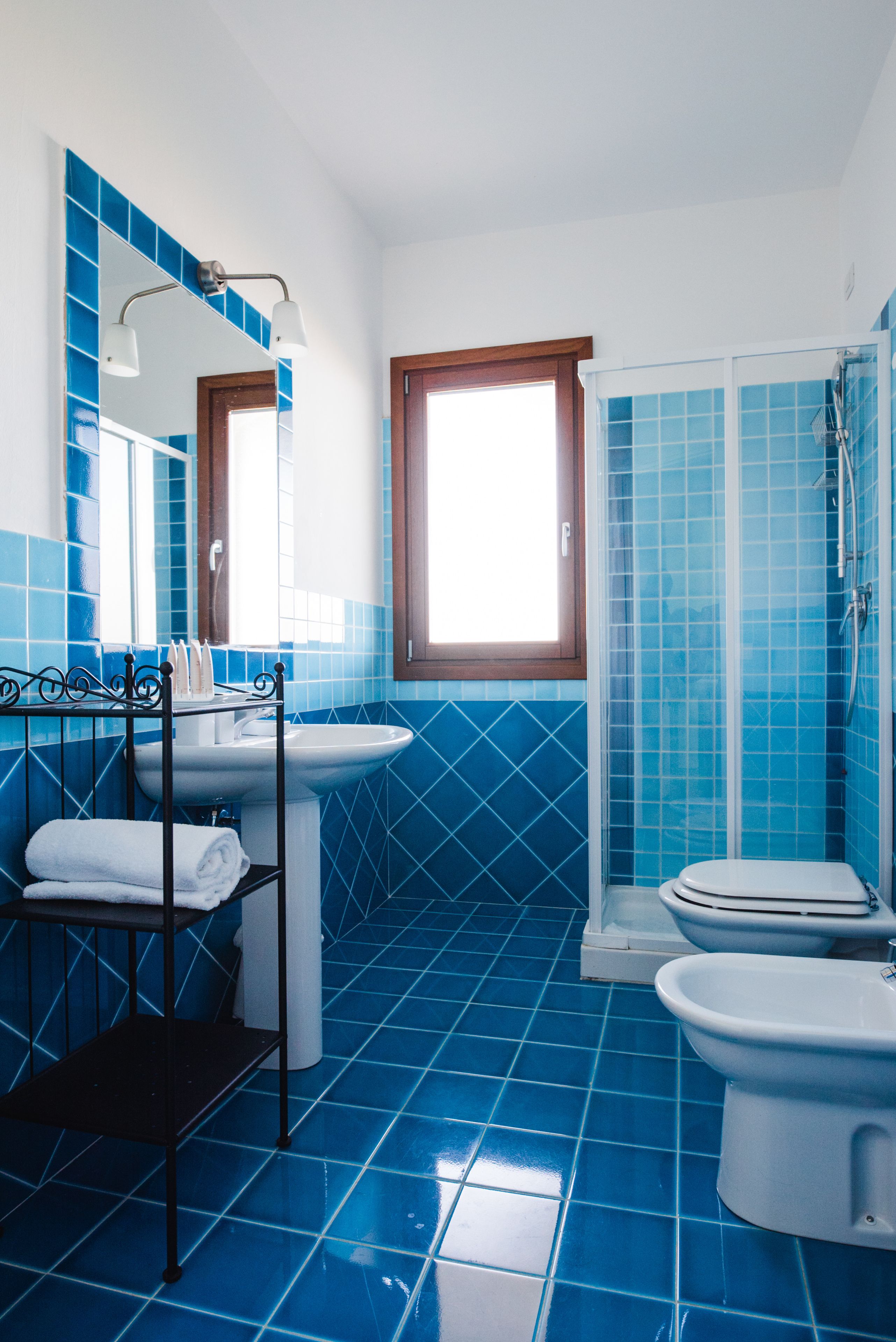 A bathroom with blue tiles, a sink, a toilet, a bidet, and a shower.