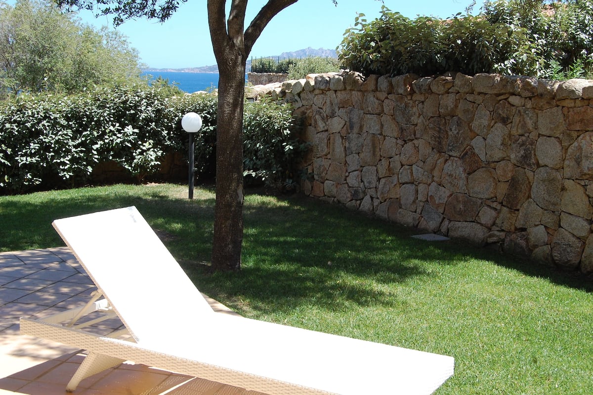 A sunlit outdoor area with a stone wall, a tree, and a lounge chair.