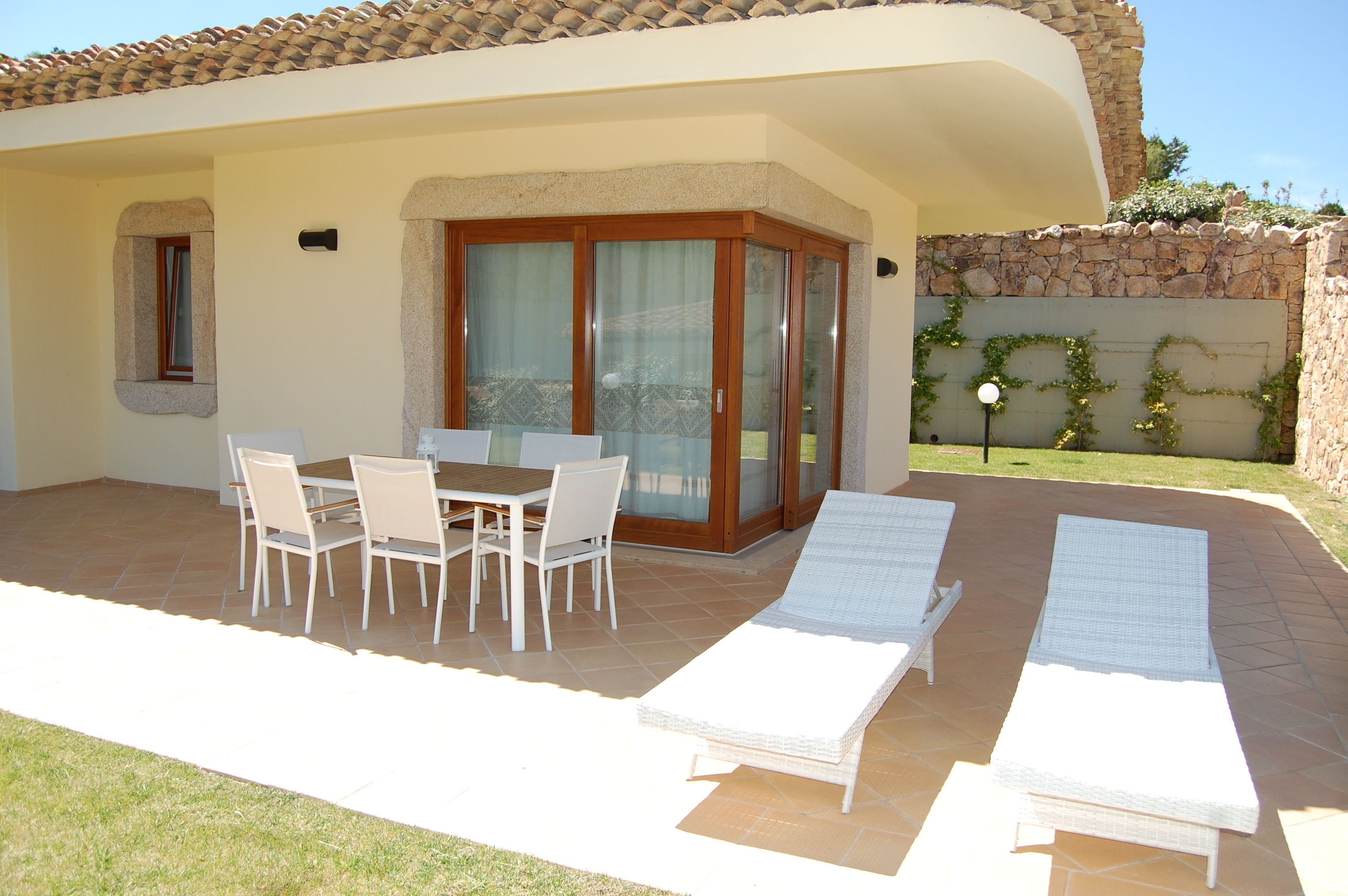 A patio with a table and chairs, a covered seating area, and two lounge chairs.
