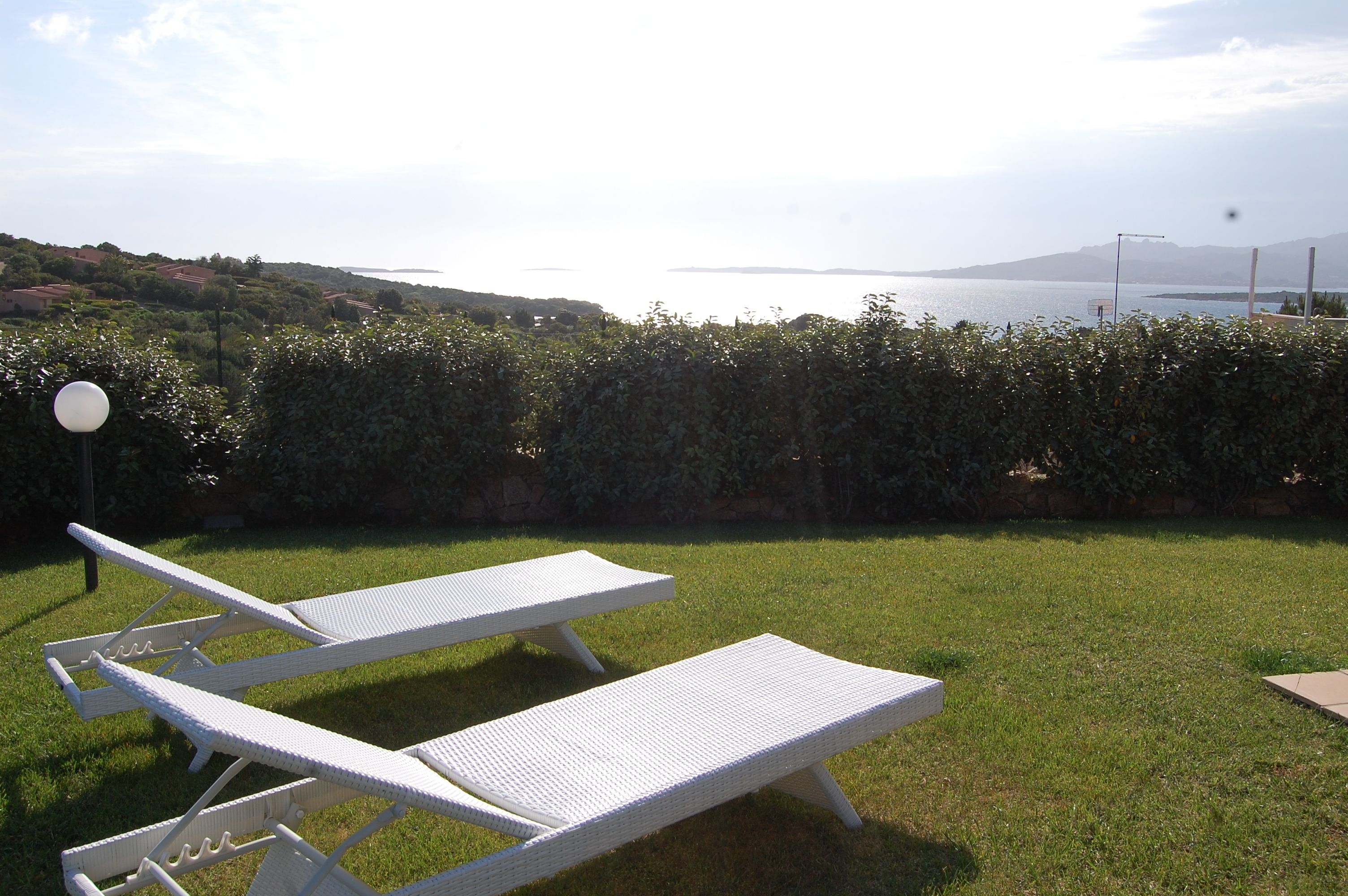 A grassy area with white lounge chairs and a view of the sea.