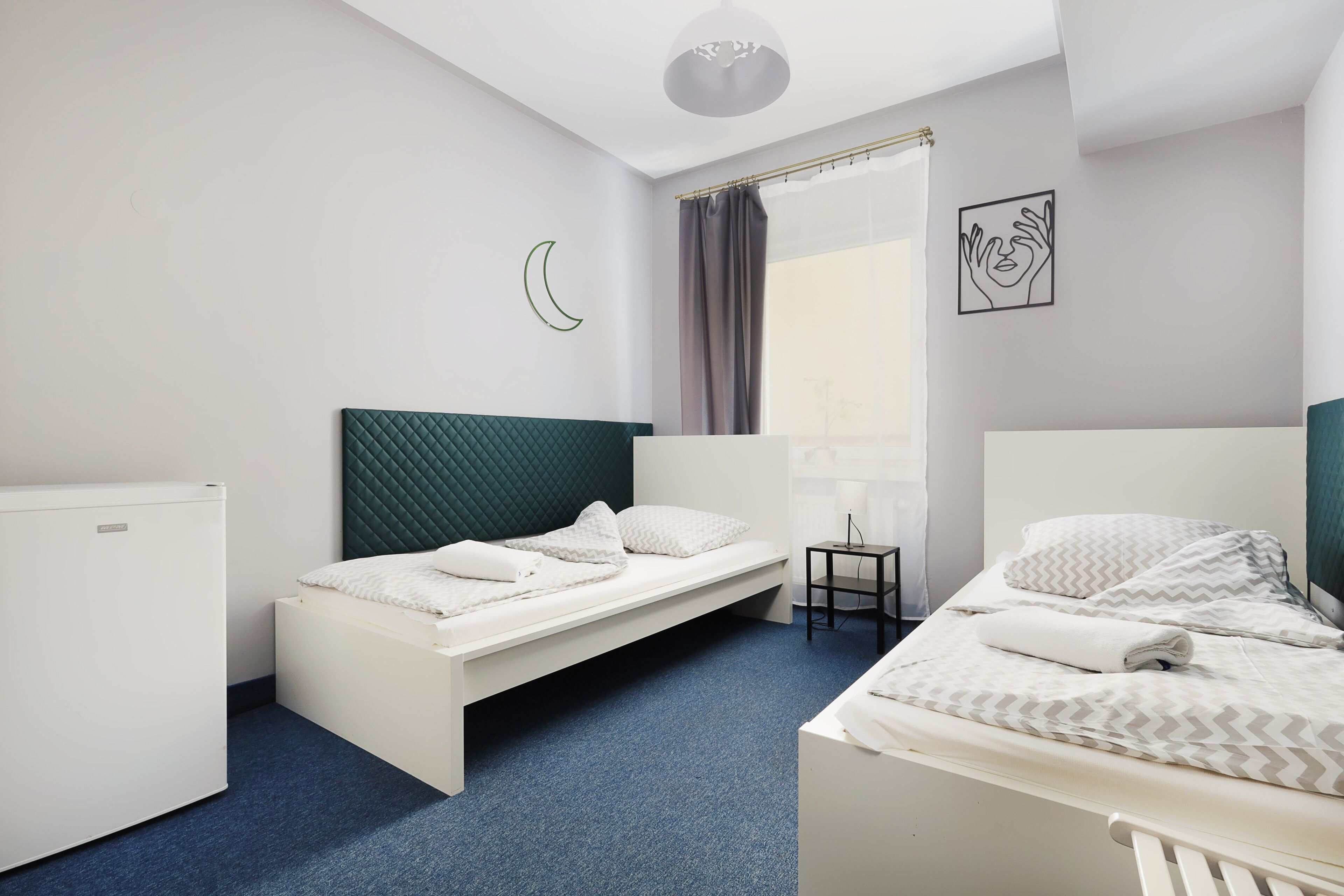 Une chambre d’hôtel de taille modeste, comprenant deux lits simples, une petite table, une chaise, un bureau et une fenêtre avec des rideaux.