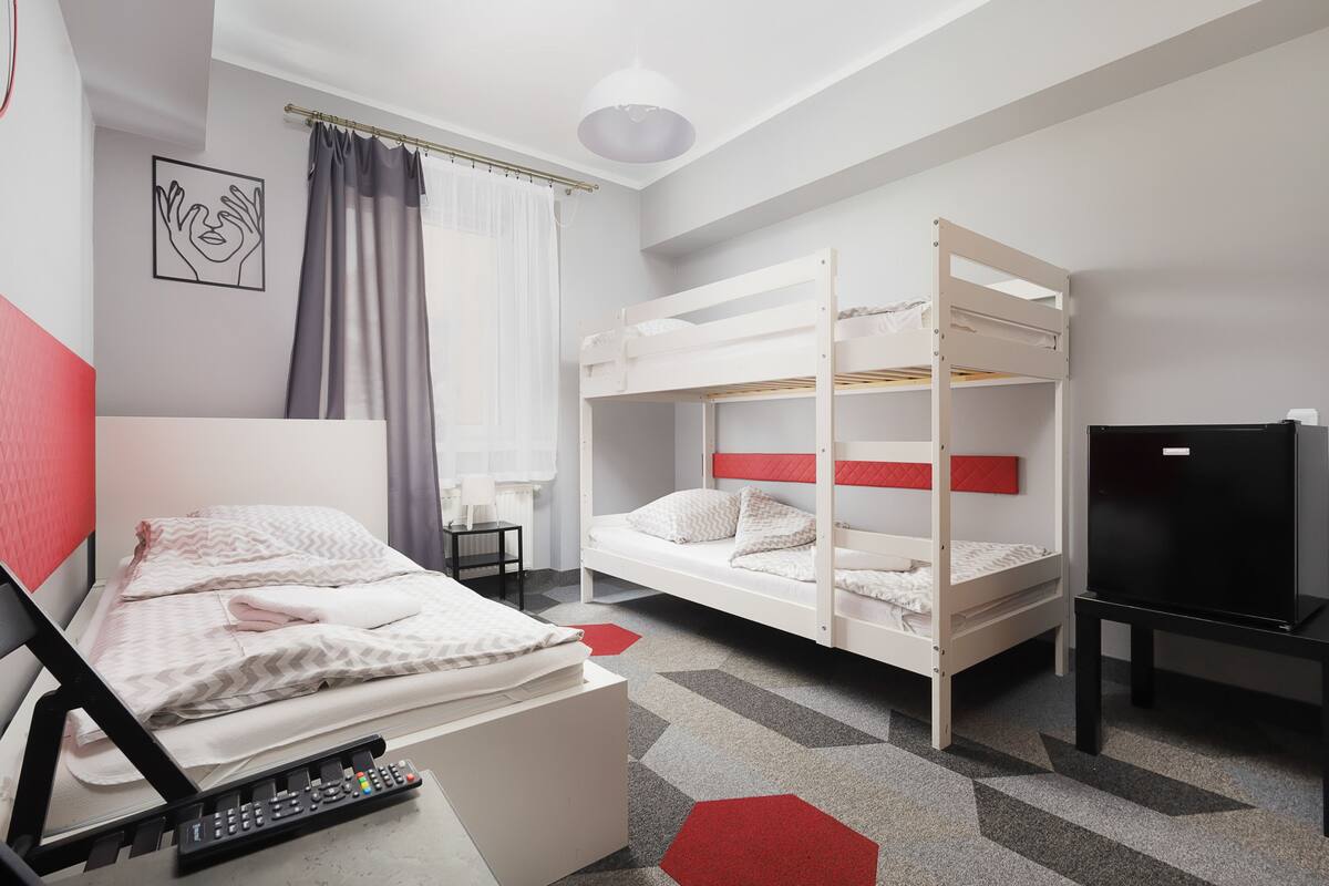Habitación de hotel con literas, una cama individual, un televisor y un escritorio con lámpara.