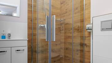 Un baño moderno con ducha de vidrio, paneles de madera, un lavamanos blanco y un inodoro.