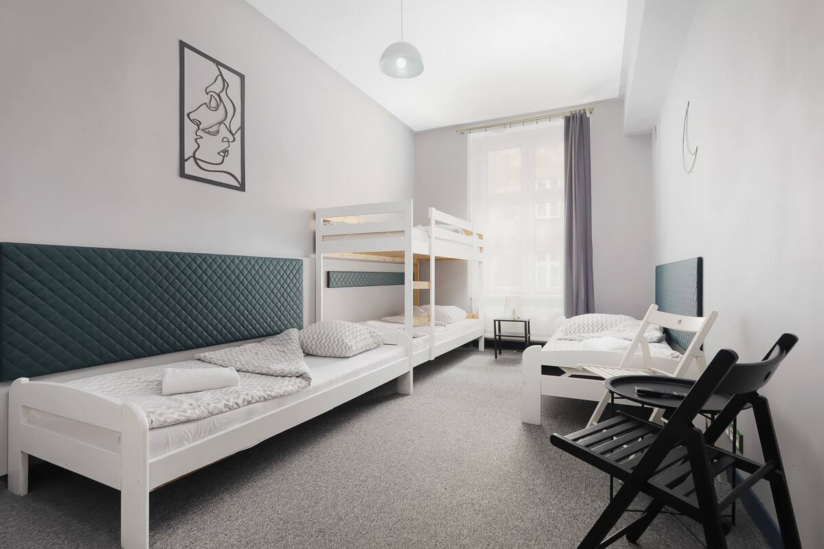 Un dormitorio moderno con una cama alta, una cama individual, un escritorio con silla y una televisión.