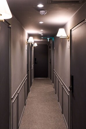 A narrow, dimly lit hallway with a carpeted floor, flanked by dark walls and doors, leading to a room with a closed door at the end. - Stay Seorae (Seoul)