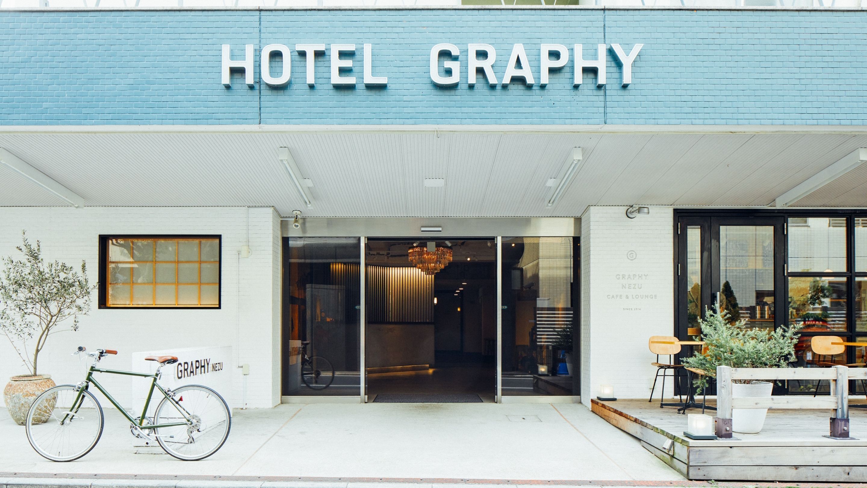 A hotel entrance with a blue facade, a bicycle parked outside, and a sign reading "HOTEL GRAPHY".