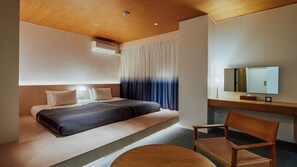 A hotel room with a bed, a desk, a chair, a round table, a mirror, and a window with curtains.