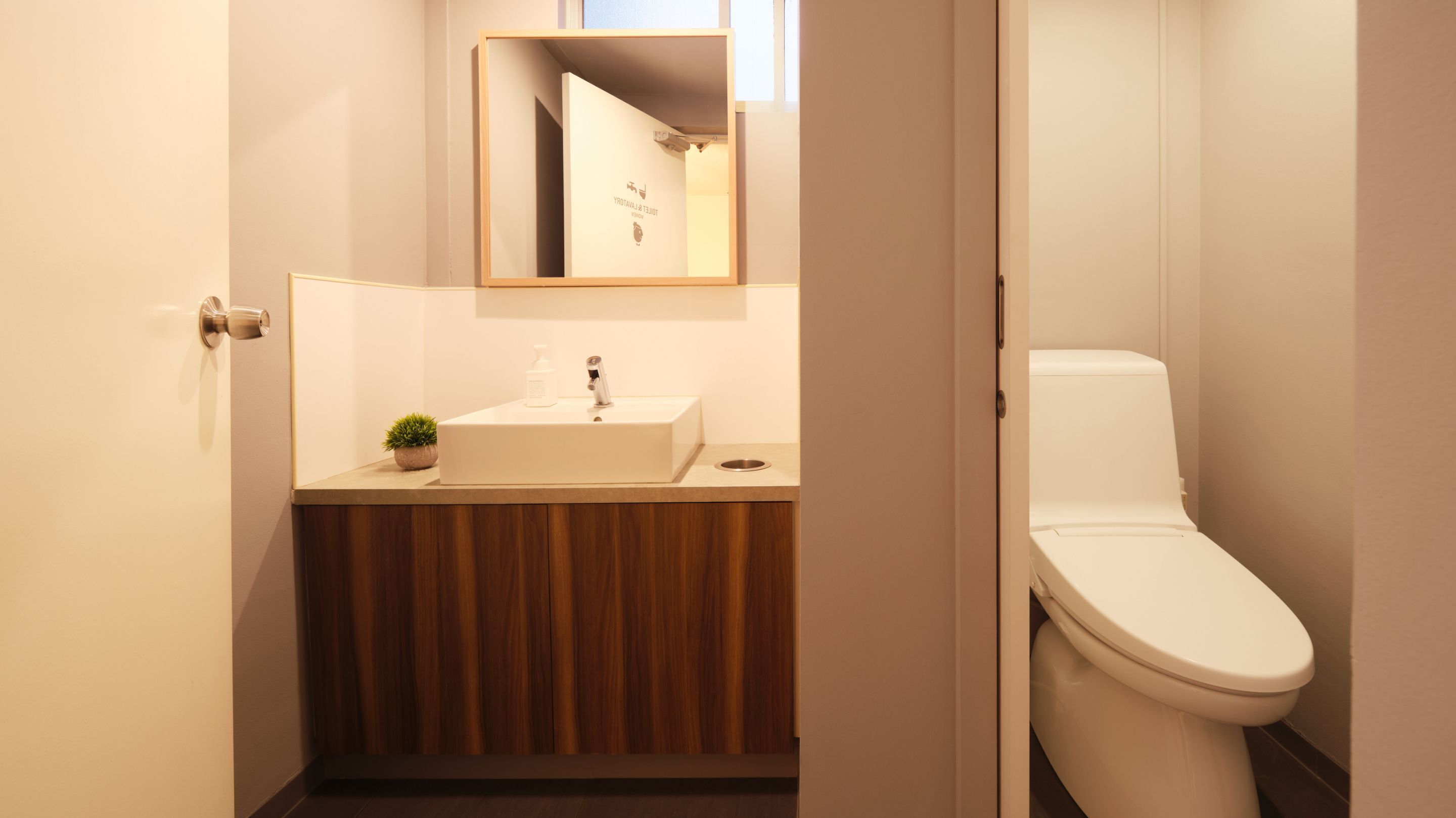 A modern bathroom with a wooden vanity, a white sink, and a toilet.