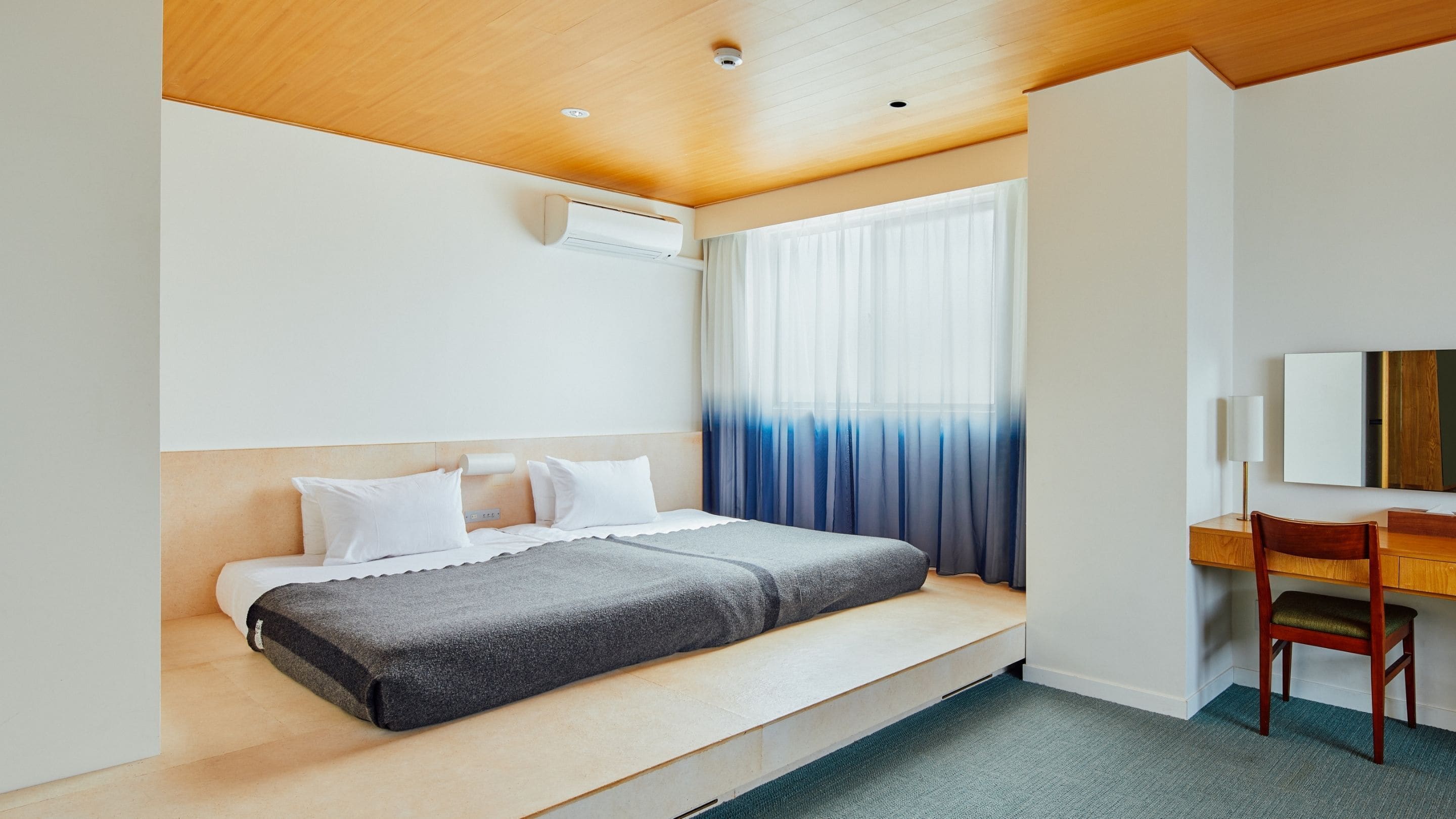 Ein Hotelzimmer mit Bett, Schreibtisch, Stuhl, Spiegel und einem Fenster mit Vorhängen.