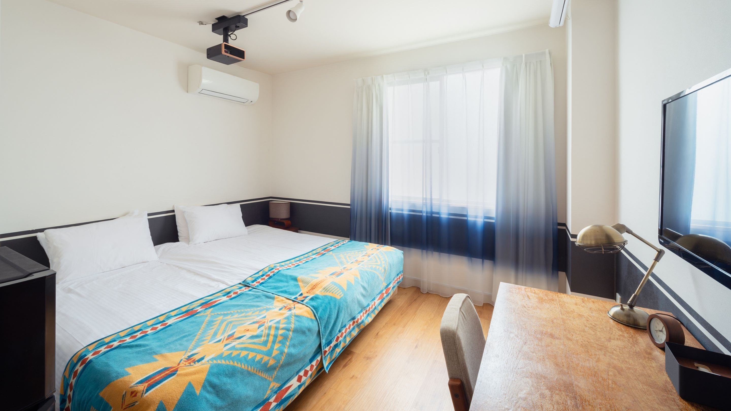 A hotel room with a bed, a desk, a chair, a TV, and a window with curtains.