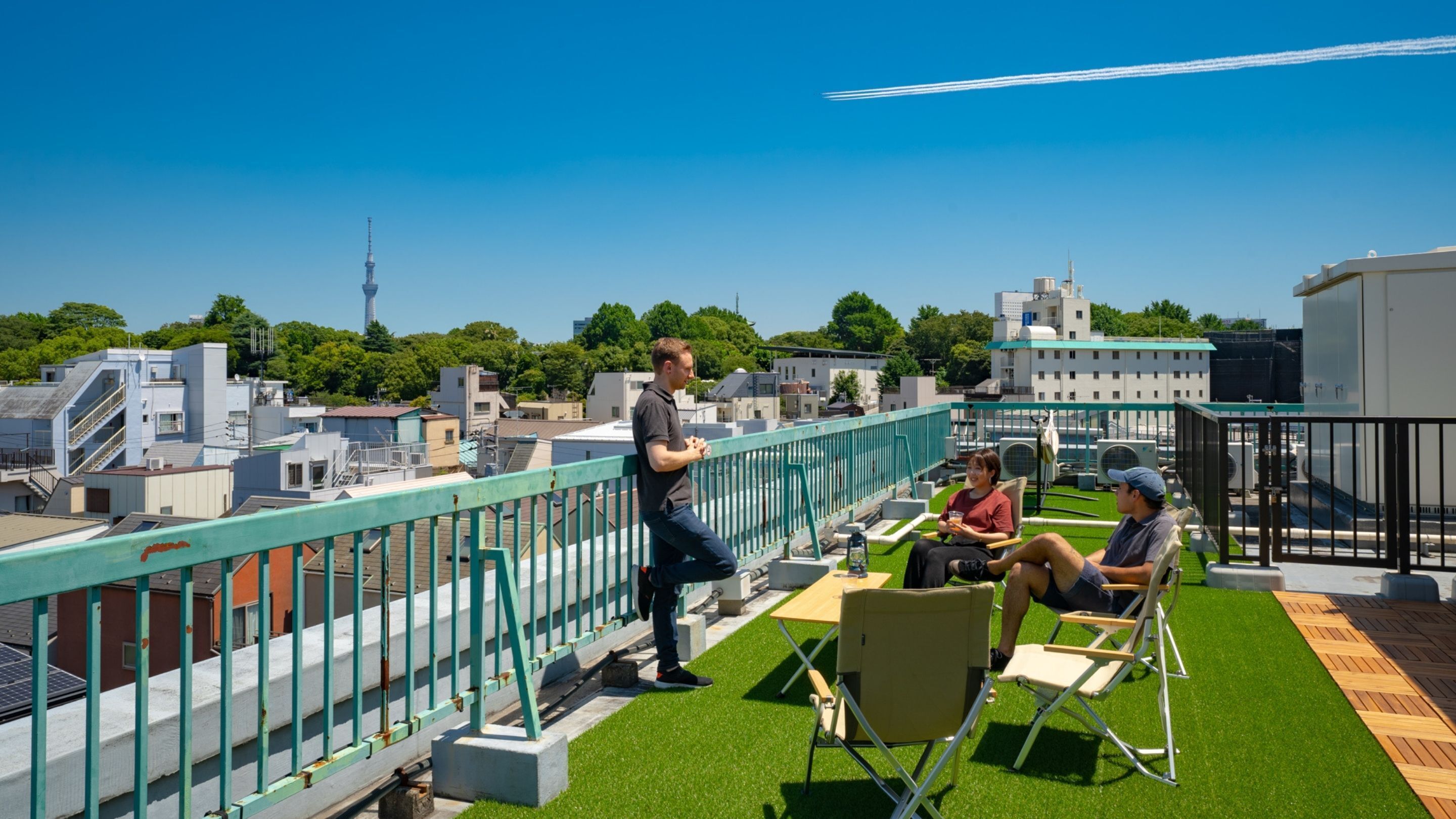 A rooftop terrace with a city view, green artificial grass, and a railing.