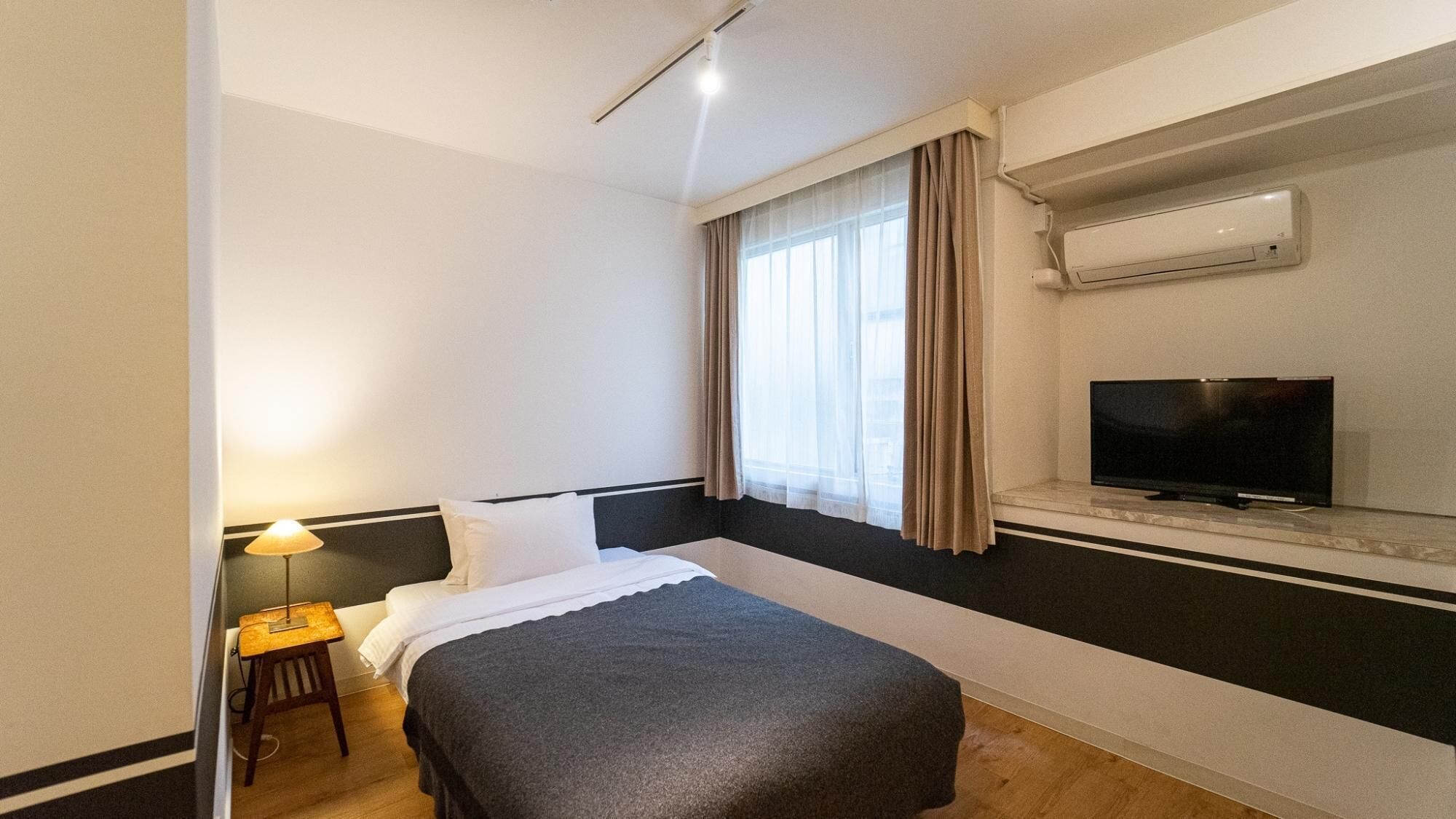 Habitació d'hotel amb llit, televisió, aire condicionat i finestra amb cortines.