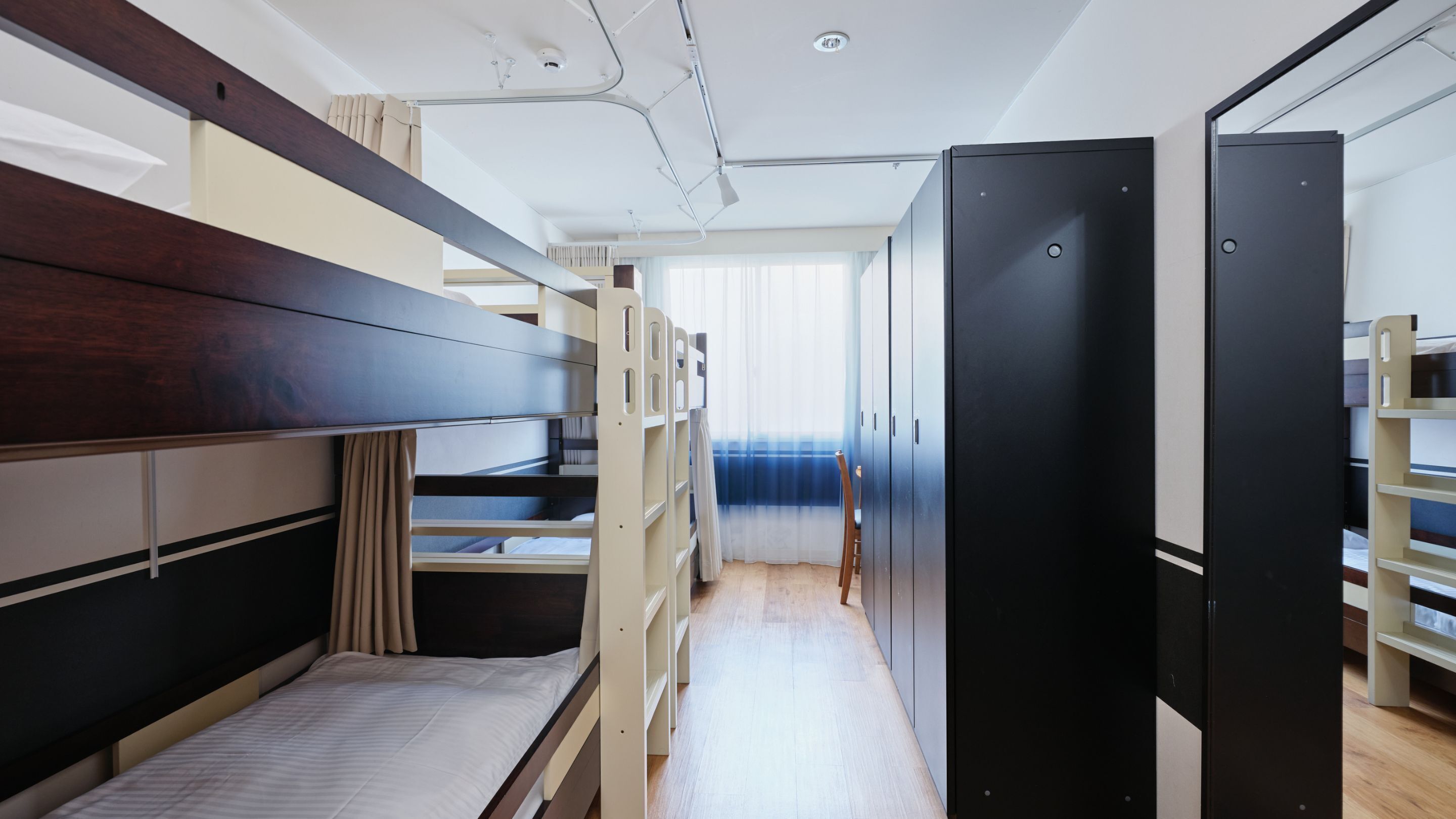 A dormitory room with bunk beds, a wardrobe, and a window with curtains.