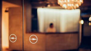 A reception area with a large, illuminated counter and directional arrows on the glass door. - Hotel Graphy Nezu (Tokyo)