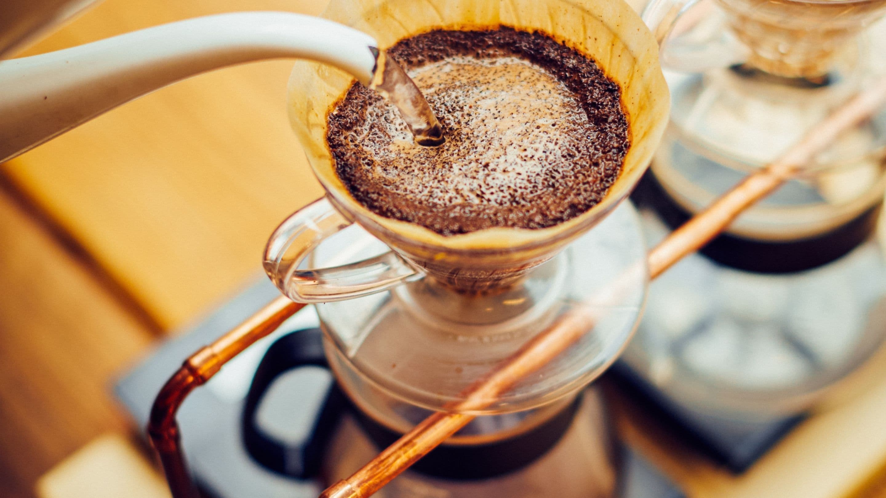 A coffee brewing station with a glass carafe and a metal spoon.