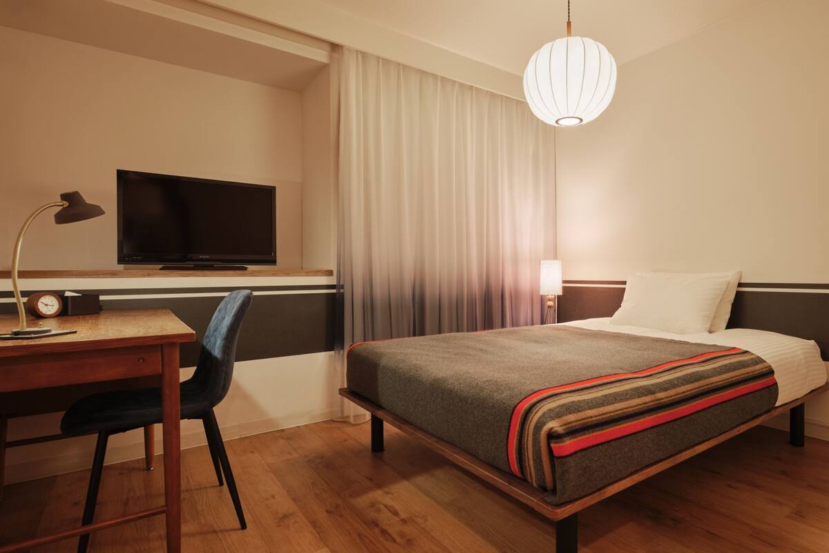 A hotel room with a bed, a desk with a computer, a TV, and a lamp.