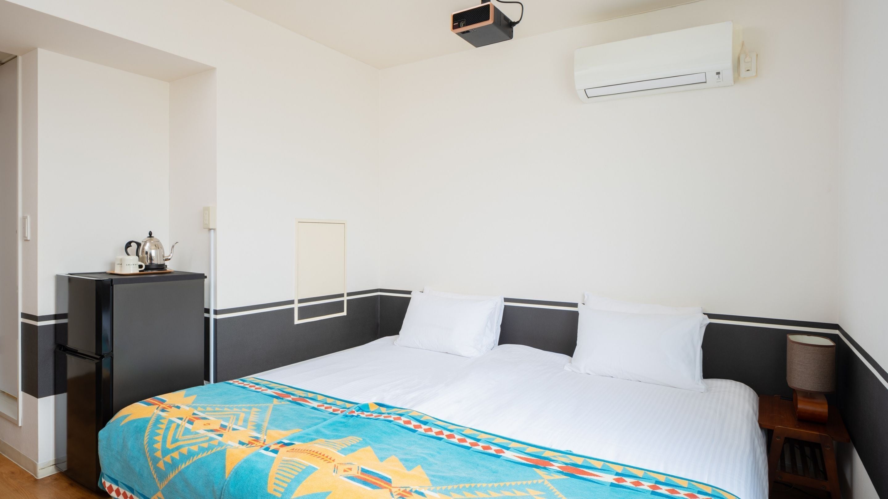 A hotel room with a bed, a desk, and an air conditioning unit.