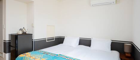 A hotel room with a bed, a desk, and an air conditioning unit.
