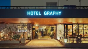 The exterior of Hotel Graphy with a prominent illuminated sign, a welcoming entrance, and potted plants around the entrance area. - Hotel Graphy Nezu (Tokyo)